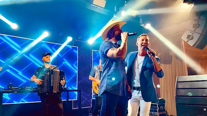Tato e Júnior cantando sob luzes azuis